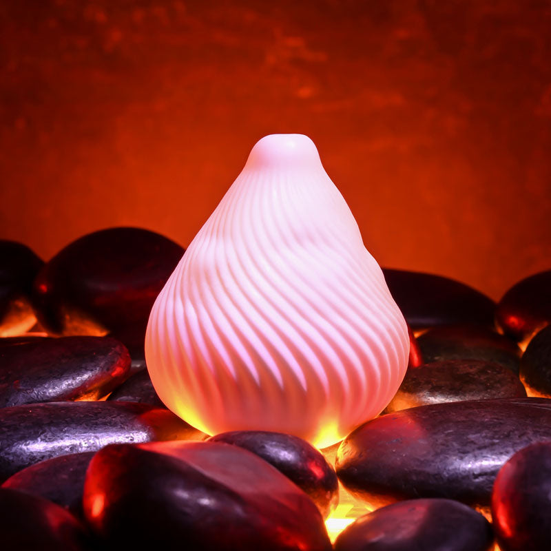 Zero Tolerance KILAUEA -  Mini Stroker Egg on smooth black stones with glowing warmth in the background.