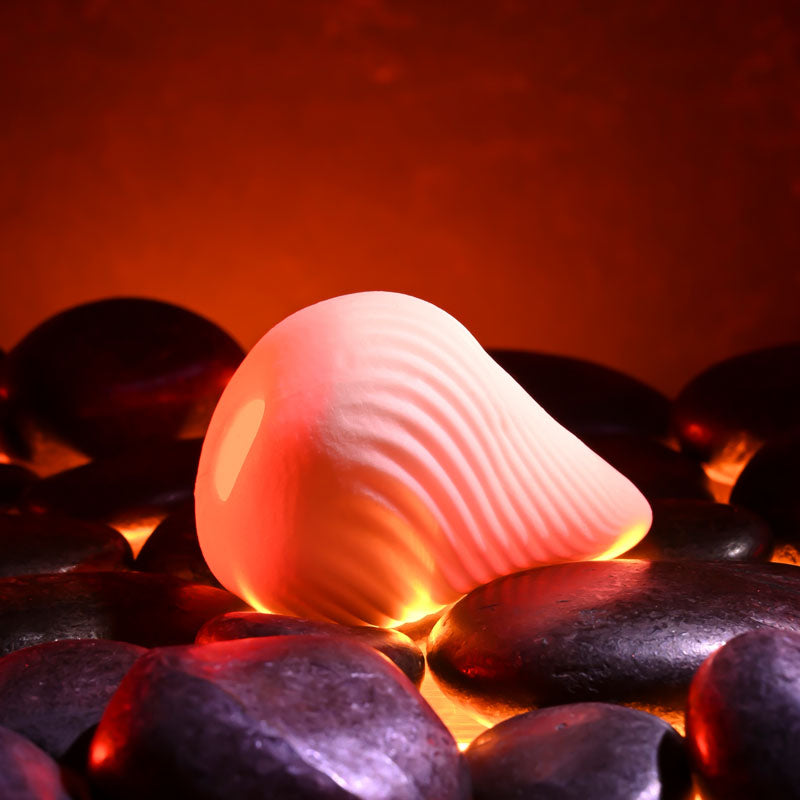 Zero Tolerance VESUVIUS -  Mini Stroker Egg sits on heated black stones, showcasing its unique swirly texture for ultimate pleasure.