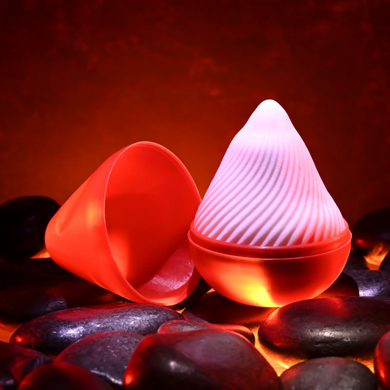 Zero Tolerance VESUVIUS -  Mini Stroker Egg resting on smooth black stones with an ambient red glow.