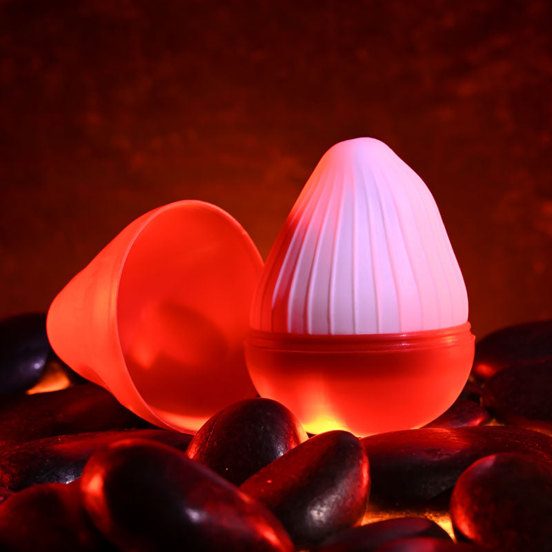 Zero Tolerance KRAKATOA -  Mini Stroker Egg displayed among black stones with a warm glow, emphasizing pleasure and intimacy.