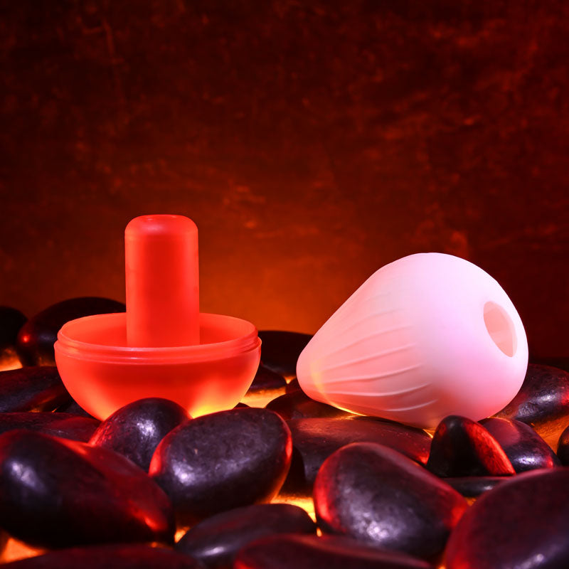 Zero Tolerance KRAKATOA -  Mini Stroker Egg resting on smooth black stones, lit with warm glowing background.