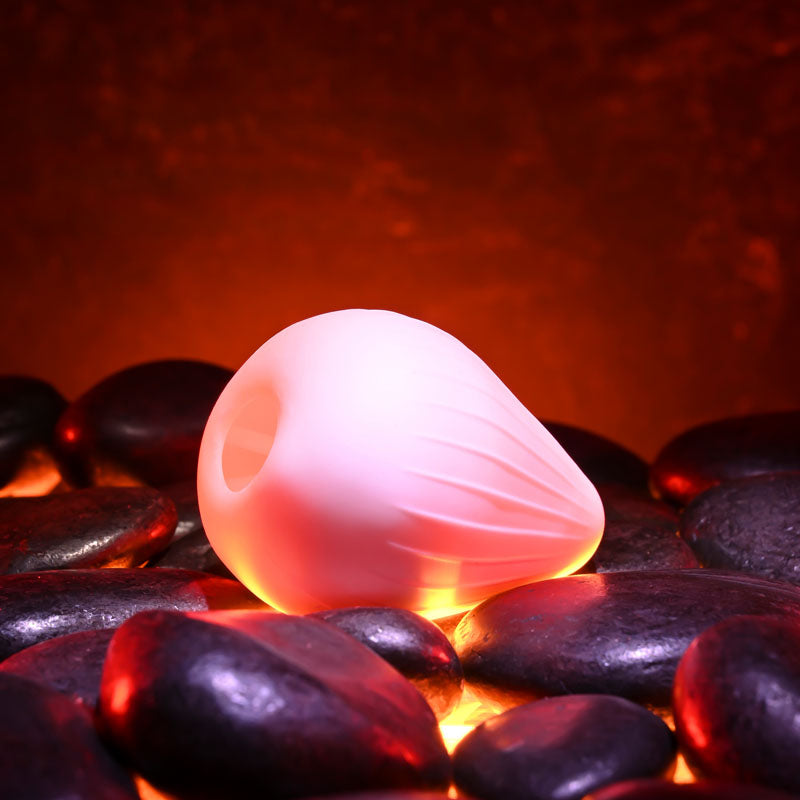 Zero Tolerance KRAKATOA -  Mini Stroker Egg resting on black stones, illuminated by warm light for intimate pleasure.